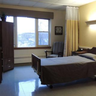 A simple hospital room with a single bed, wardrobe, and window.