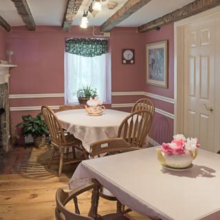 A cozy dining room with round tables and wooden chairs, featuring pink walls and decorative ceiling beams.