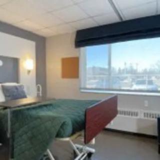 A well-lit hospital room with a bed and a large window overlooking the cityscape.