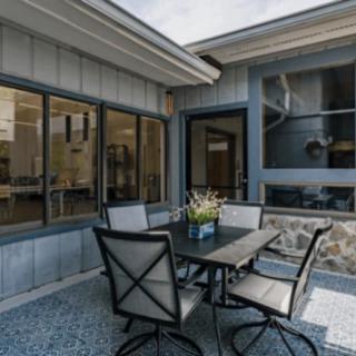 A cozy outdoor patio area featuring a dining table with chairs, surrounded by large windows and decorated with a flowerpot.