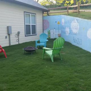 A cozy backyard with colorful chairs, a fire pit, and a mural on the fence.