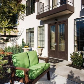 A stylish patio with green-cushioned seating in front of a modern home entrance.