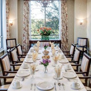 An elegantly set formal dining table with floral centerpieces and a view through large windows.