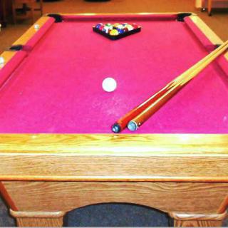 A pink-felt pool table with racked balls and cue sticks ready for play.
