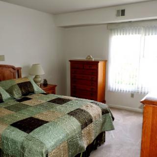 A cozy bedroom featuring a quilted bedspread, wooden furniture, and natural light from a window.