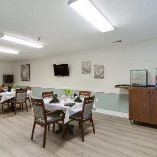 A neatly arranged dining room with tables set for service, featuring modern decor and a television mounted on the wall.