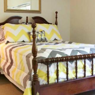 A cozy bedroom with a wooden bed frame and yellow chevron patterned bedding.