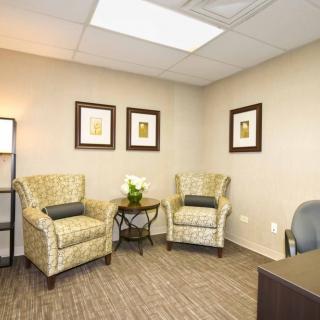 A cozy office space with two patterned chairs, a small table, and framed artwork on the wall.