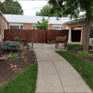 A serene garden area featuring a pathway, bench, and surrounding greenery.