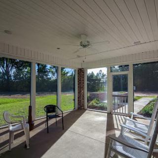 A sunlit, screened-in porch with chairs and outdoor views.