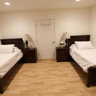 A cozy bedroom featuring two beds, bedside tables with lamps, and a warm wooden floor.