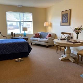 A cozy bedroom and living area with a bed, sofa, table, and chairs set near a large window.