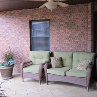 Outdoor patio with brick wall, cushioned chairs, and a potted plant.