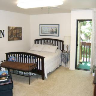 A cozy bedroom with a double bed, decorated with framed artwork and featuring a doorway leading to a balcony.