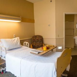 A tidy hospital room with a single bed and a small table for patients.