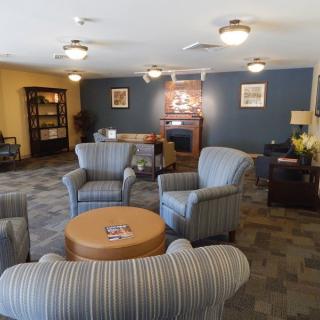 A cozy living room with striped armchairs, a round wooden table, and a bookshelf in the background.