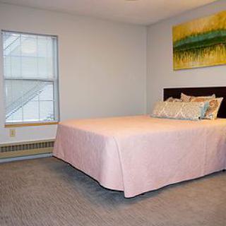 A simple bedroom with a pink-covered bed, a window, and decorative artwork.