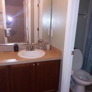 A small bathroom with a sink and mirror, adjacent to a toilet and shower area.