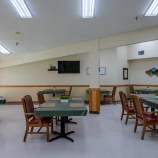 A well-lit dining area with several tables and chairs, featuring a wall-mounted television.