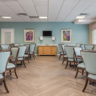 A modern dining room with neatly arranged tables and chairs, featuring art on the walls and a television.