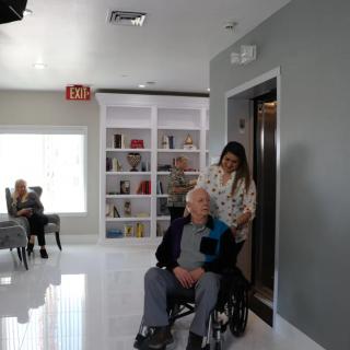 A caregiver assists an elderly person in a wheelchair in a nursing home setting.