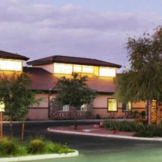 A building illuminated by soft evening lights with surrounding trees and a cloudy sky.