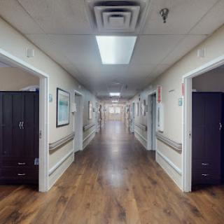 A well-lit corridor in a hospital, featuring polished wooden floors and doors to patient rooms.