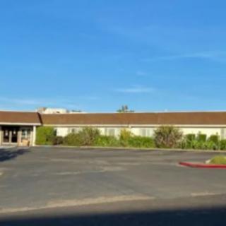 A wide, single-story building with a parking lot in the foreground and clear blue sky above.