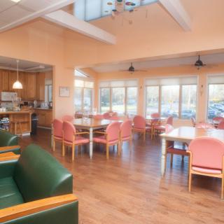 A bright and spacious dining area with a kitchen, featuring tables and chairs near large windows.