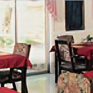 Cozy restaurant interior with tables and chairs covered in red tablecloths.