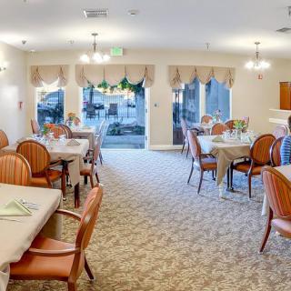A well-lit dining area with neatly arranged tables and chairs, featuring large windows and elegant decor.