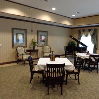 A cozy dining or social area with tables and chairs, complemented by a grand piano and elegant wall decorations.
