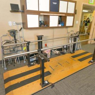 A rehabilitation clinic room featuring parallel bars and various medical equipment for physical therapy.