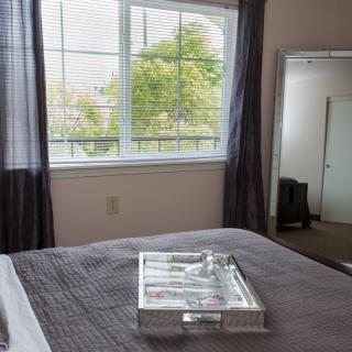 A cozy bedroom with a large window, a mirror, and a neatly made bed featuring a decorative tray.