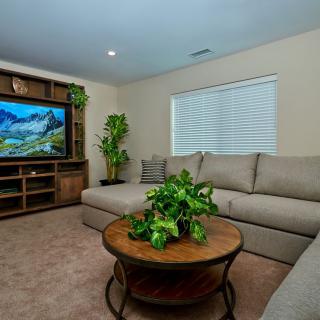 A cozy living room with a large sectional sofa, flat-screen TV, and indoor plants.