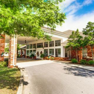 A sunny view of a building entrance with trees and a driveway.