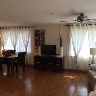 A cozy living and dining area featuring hardwood floors, a television, and ample natural light through the curtains.