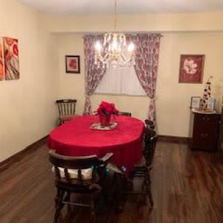 A cozy dining room with a red tablecloth and wooden chairs, featuring a chandelier and decorative artwork.