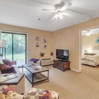 A cozy living room with a sofa, coffee table, television, and a view into an adjacent bedroom.