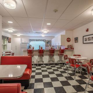 A retro diner interior featuring red chairs, booth seating, and a black-and-white checkerboard floor.