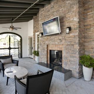 A modern outdoor patio with a stone fireplace and seating area, featuring a wall-mounted TV.