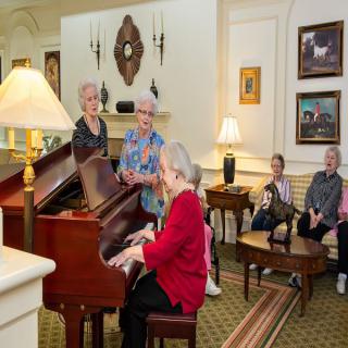 A group of seniors enjoying a piano performance in a cozy living room setting.