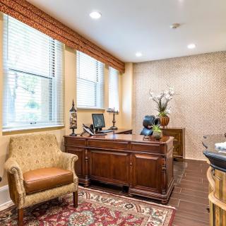 A well-decorated office space with a wooden desk, upholstered chairs, and a patterned carpet.
