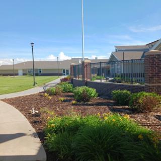 A well-maintained outdoor area featuring a pathway, garden beds, and buildings under a clear blue sky.