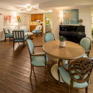 A cozy living area featuring a round dining table, elegant chairs, and a piano, complemented by wooden flooring and tasteful home decor.