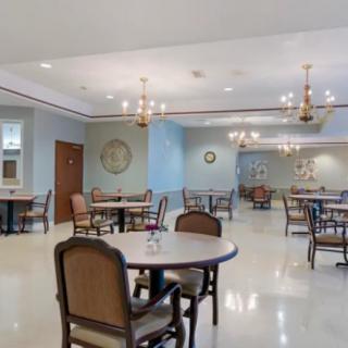An empty dining room with neatly arranged tables and chairs, illuminated by elegant chandeliers.