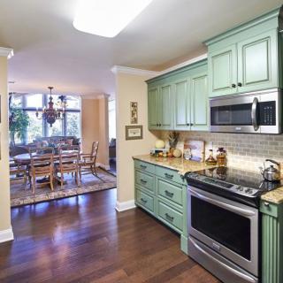 A modern kitchen with green cabinets opening into a dining area with hardwood flooring.