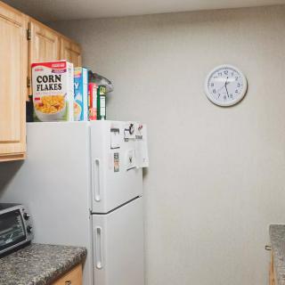 A kitchen corner with a refrigerator topped with cereal boxes, a wall clock, and cabinets above a countertop with a toaster oven.