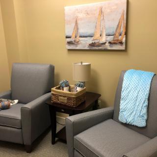 A cozy waiting room with two gray chairs and a seaside painting.