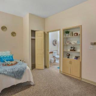 A cozy bedroom with an open closet, adjoining bathroom, and decorative shelving.